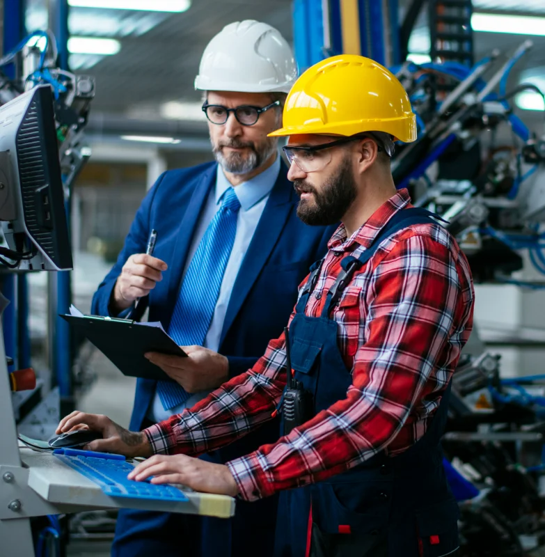 Two asset maintenance faculties in hard hats and
                  overalls working on a machine