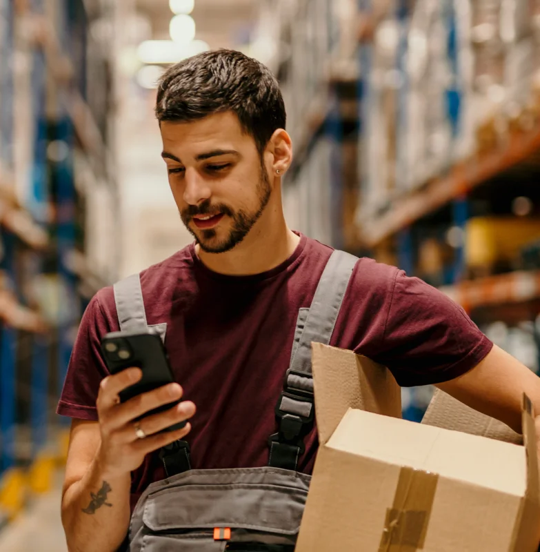 An Inventory management employee in a warehouse looking
                  at his cell phone